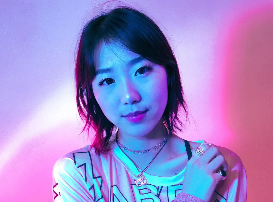 A woman with a subtle smile lit by pink and blue neon lights, exuding a cool, modern vibe gnerated with EraseID.